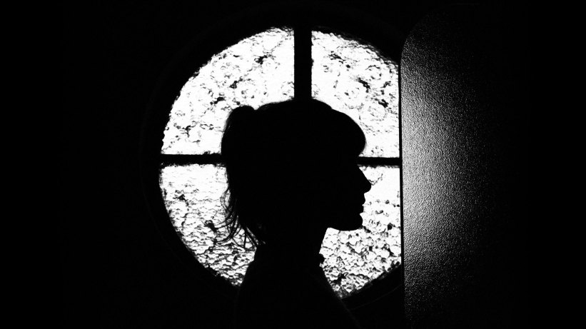 Silhouette of a young woman in front of cross-shaped window lighting.