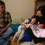 A father, mother, daughter, and baby sitting on bunk beds in a shelter in Praia Grande, Brazil.