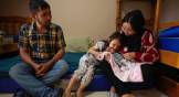 A father, mother, daughter, and baby sitting on bunk beds in a shelter in Praia Grande, Brazil.